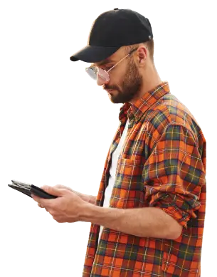 A man dressed in a plaid shirt and hat gazes at his phone, focused on the screen in front of him.